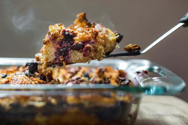 Baked French Toast Recipe with Michele's Lemon Pistachio Granola topping being served from a glass dish, steam rising.
