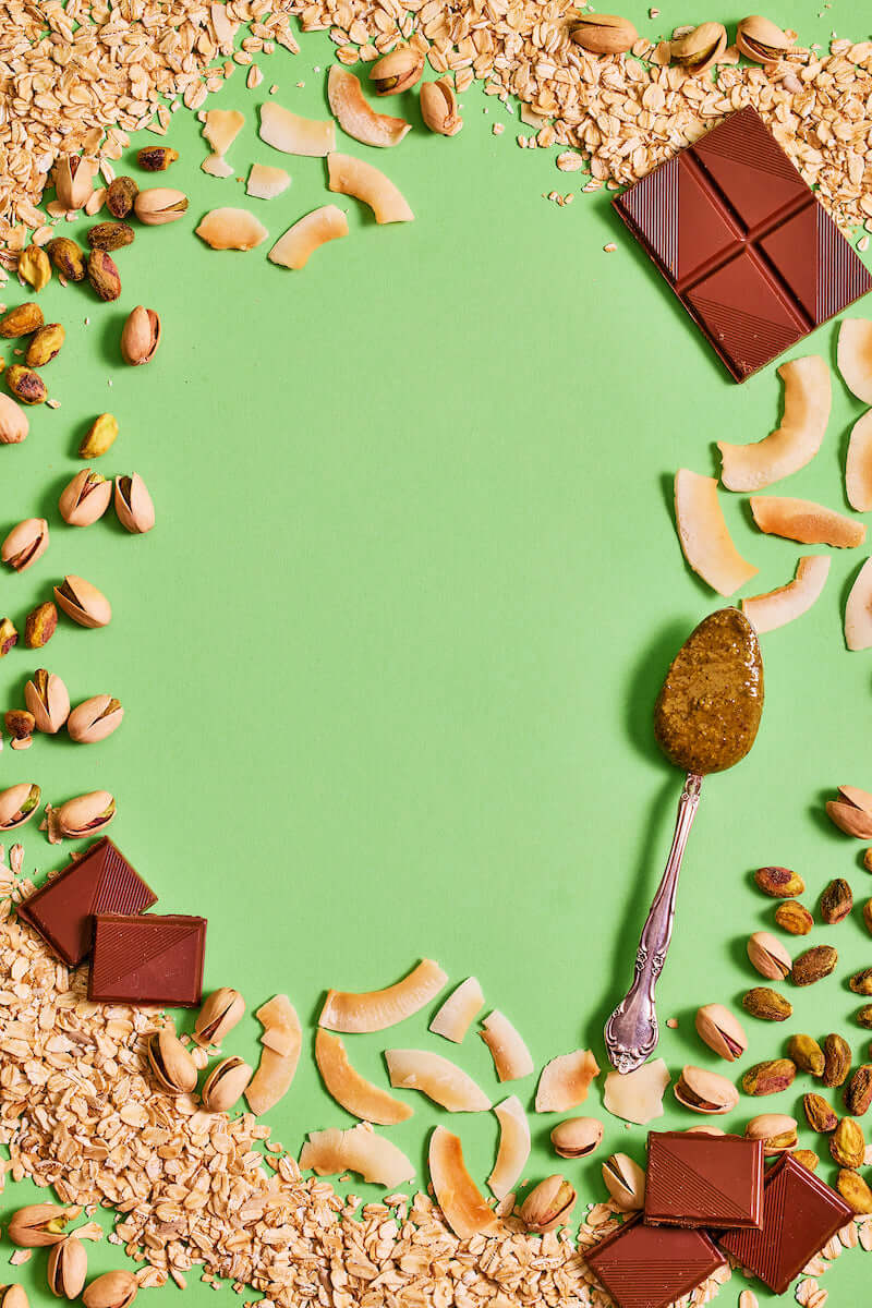 Michele's Granola chocolate pieces, nuts, and a spoon with a green background